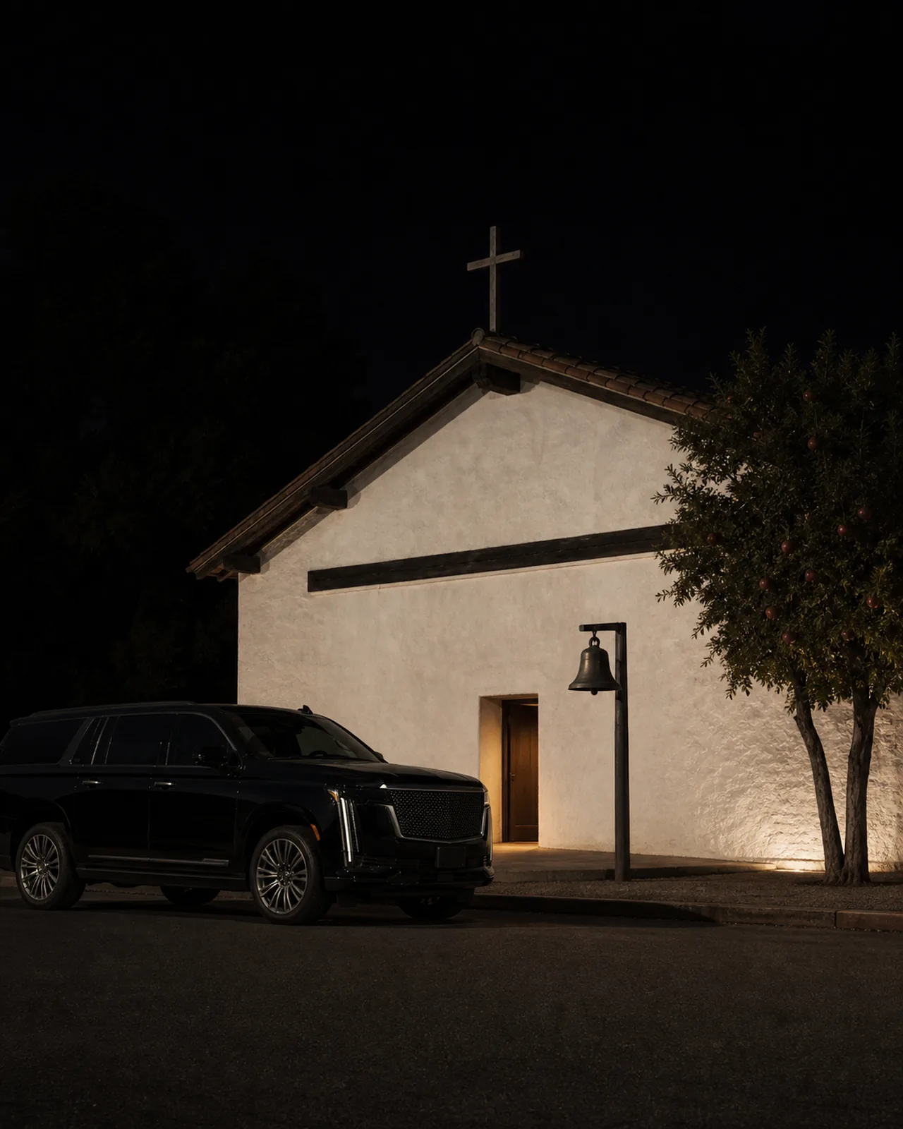 A black Cadillac Escalade ESV beside the white adobe Mission San Francisco Solano at dusk.